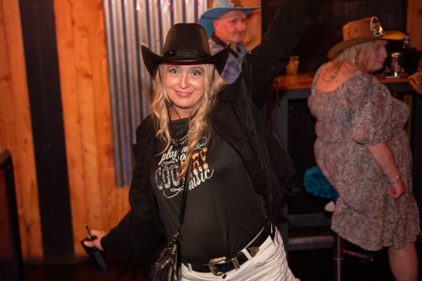 A woman in a black cowboy hat and fringed jacket dancing in a nightclub.