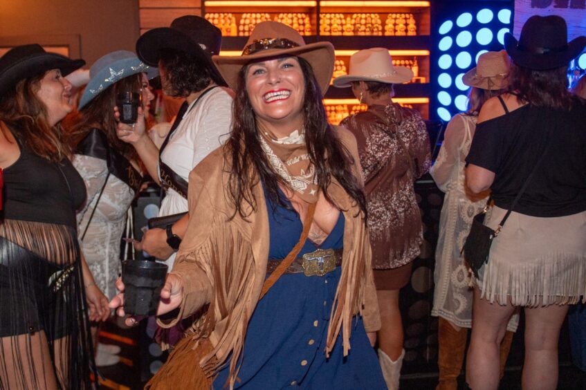 A woman in a cowboy hat and tasselled coat dances beside the bar in a nightclub. 
