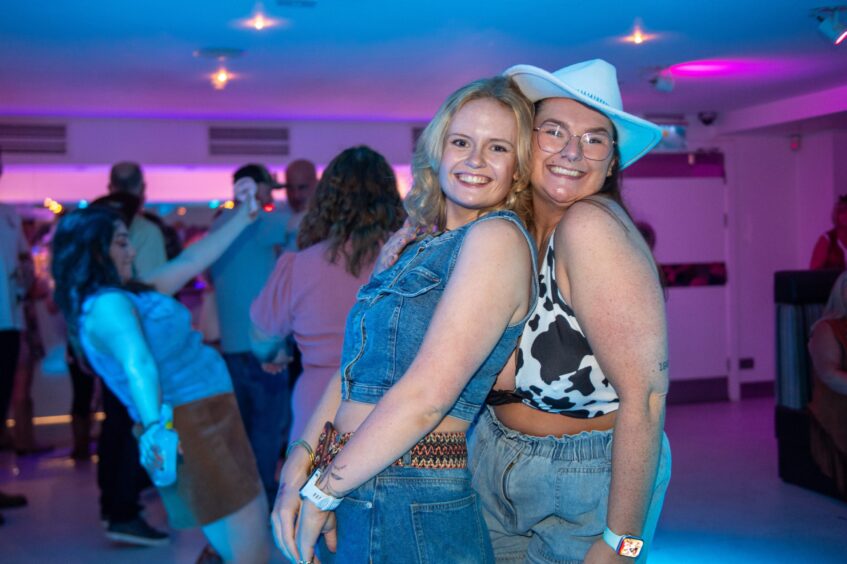 Two women in country-and-western garb pose in a nightclub. 
