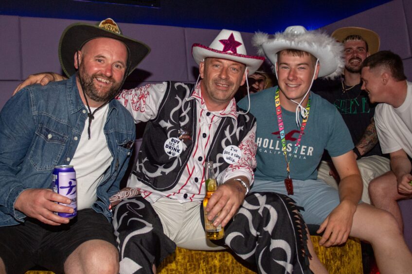 Men in country-and-western garb pose in a nightclub. 
