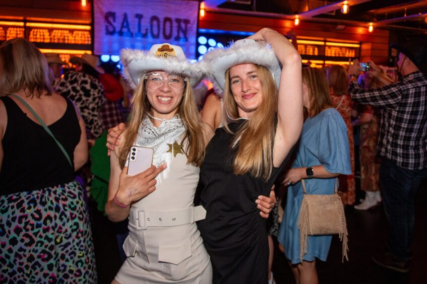 Two women in fur-trimmed cowboy hats among dancers in a nightclub. 