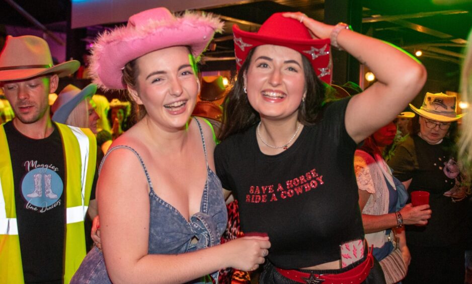 Two women in cowboy hats share a laugh in a nightclub. 