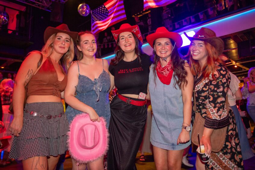 Five women with cowboy hats in a nightclub. 