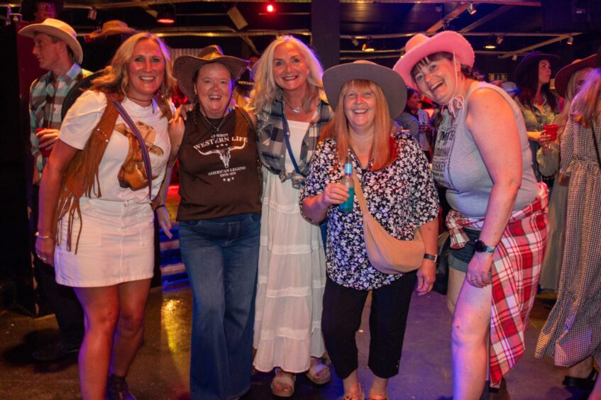 Five women, three of them in cowboy hats, pose in a nightclub. 