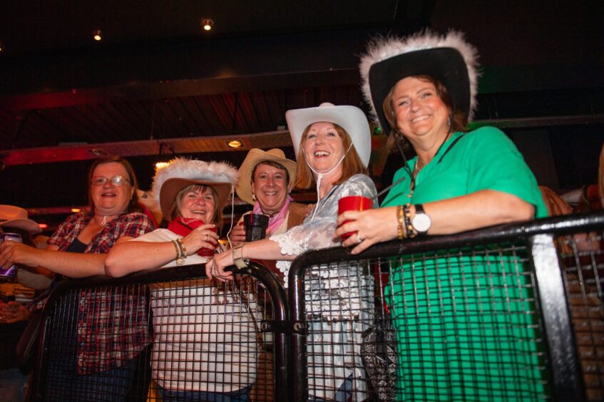 Women in cowboy hats smiling in a nightclub. 