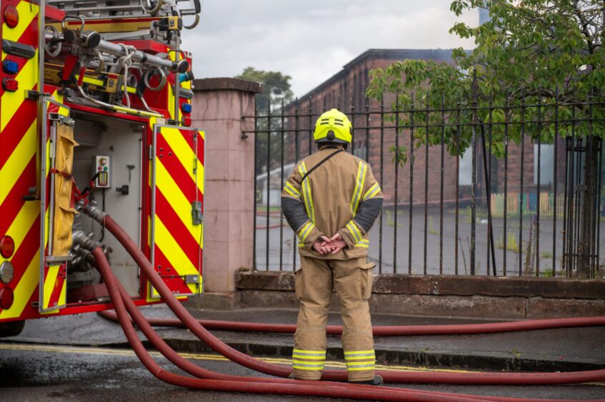 Firefighter with back to camera in front of burned out Balhousie Primary School