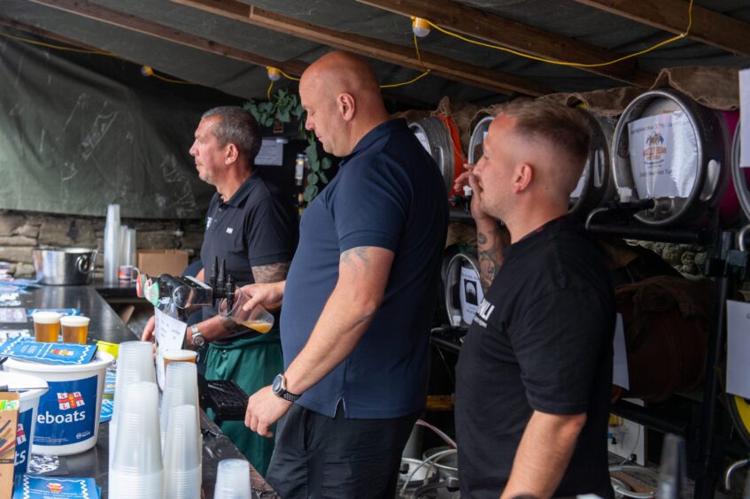 Three men serving drinks from a bar within a tent. 