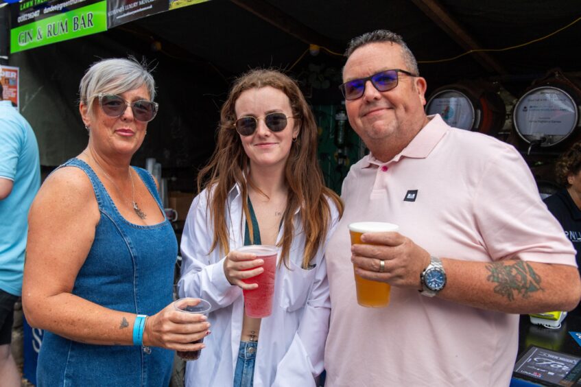 Two women and a man, all in sunglasses and clutching drinks. 