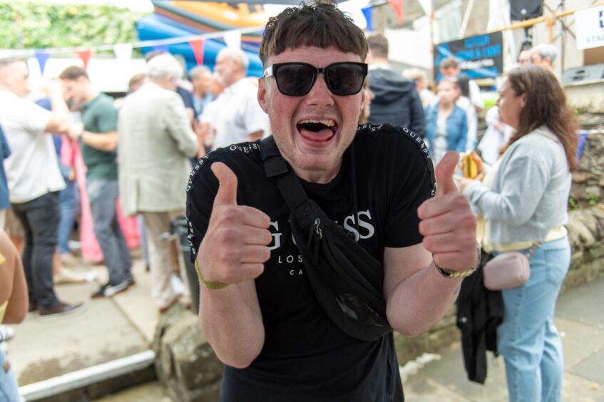 A man in T-shirt and sunglasses does the thumbs up. 