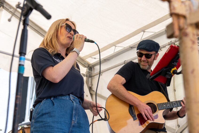 A woman singing into a microphone while a man plays an acoustic guitar. 
