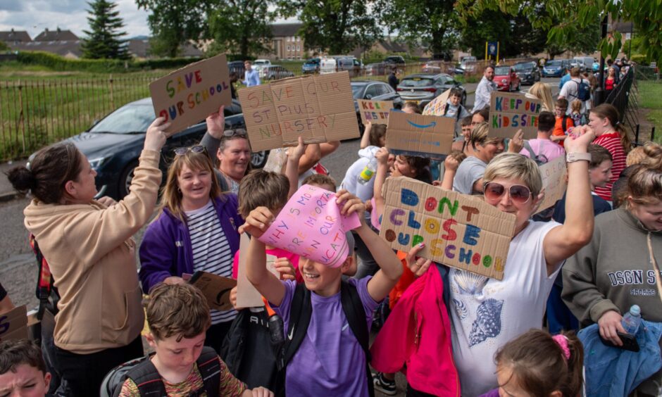 Adults and children holding placards outside a school. 
