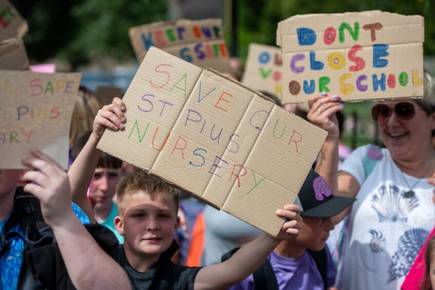 A boy with a placard that reads 'Save our St Pius nursery' amid a group of other protesters. 