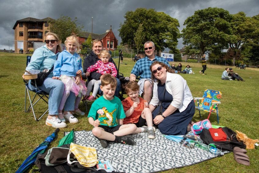 Families sit on the grass to listen to music