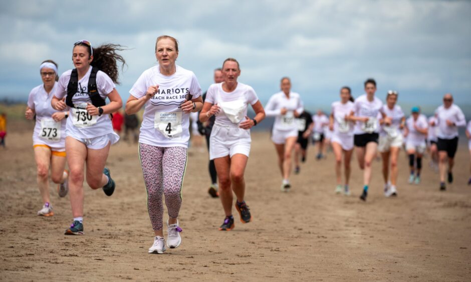 A group of women in white t-shirts enjoy their run on the sand