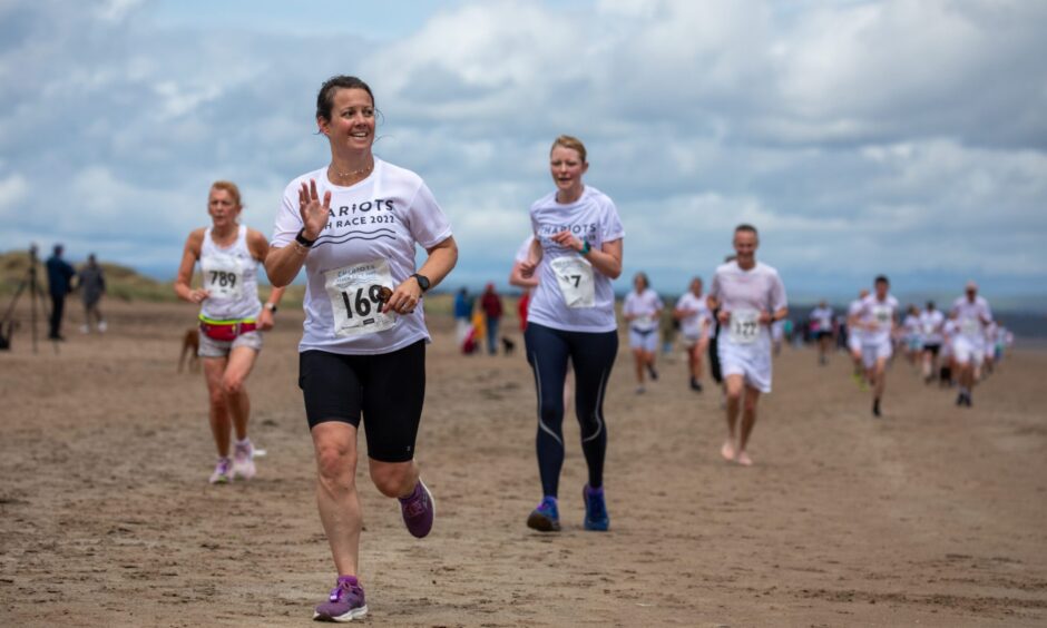 A female competitor waves to the crowd as she runs along the beach