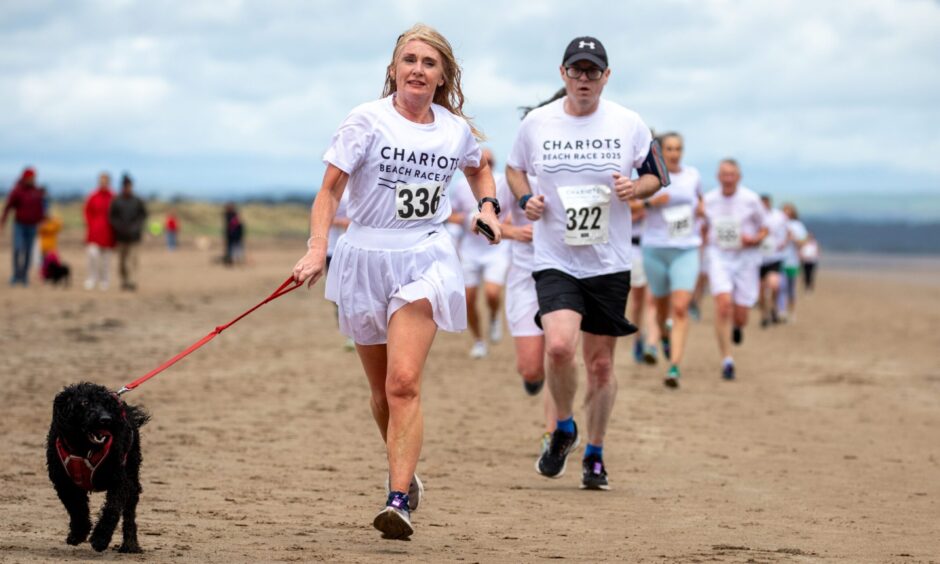A black dog on a lead joins in the fun at the Chariots of Fire beach race in St Andrews