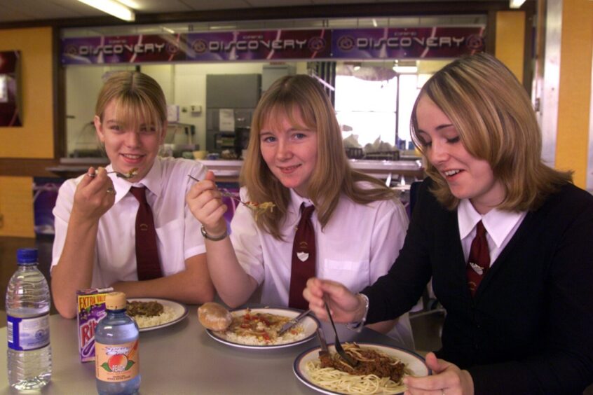 Three pupils sitting at a table and enjoying a lunchtime meal. 