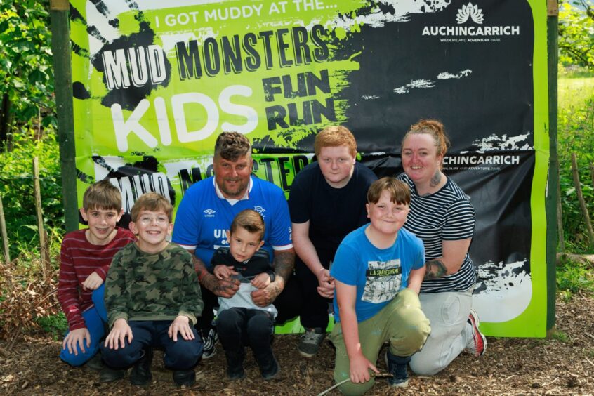Adults and children pose at the Mud Monkeys Family Fun Run banner. 