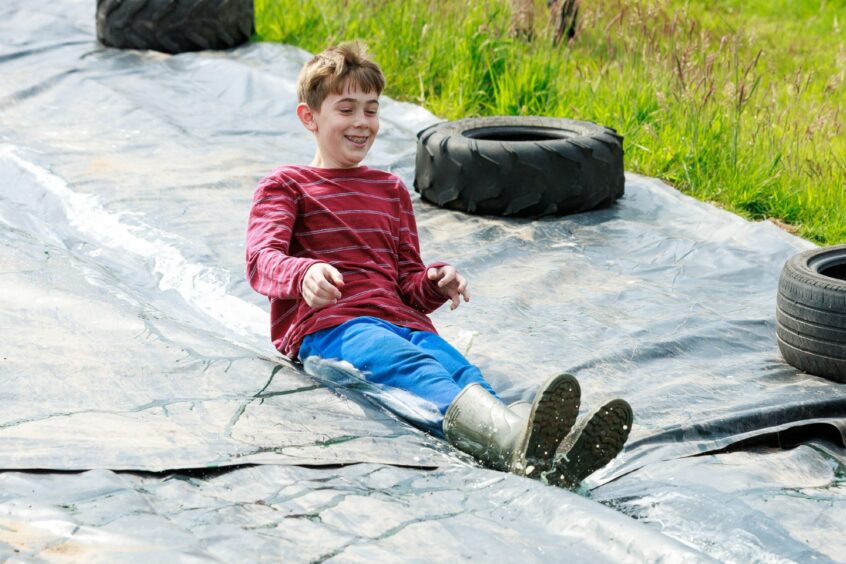 A boy slides down a tarpaulin held in place on either side by tyres. 