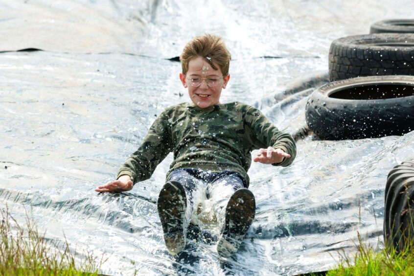 A boy slides down a tarpaulin held in place on either side by tyres. 
