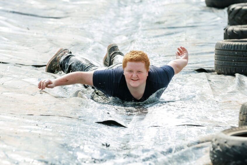A boy slides down a tarpaulin held in place on either side by tyres. 