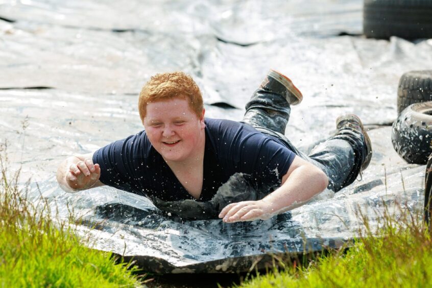 A boy slides down a tarpaulin held in place on either side by tyres at the Mud Monkeys Family Fun Run.