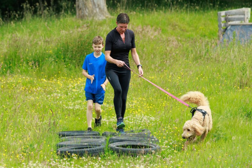 A woman, boy and dog tackle the obstacle of tyres on the ground. 