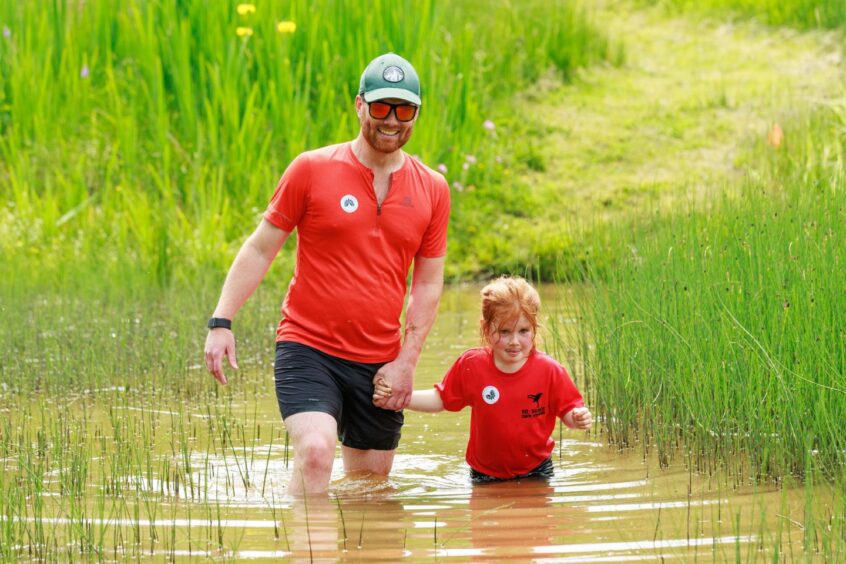 A man and young girl wade through a muddy pond. 