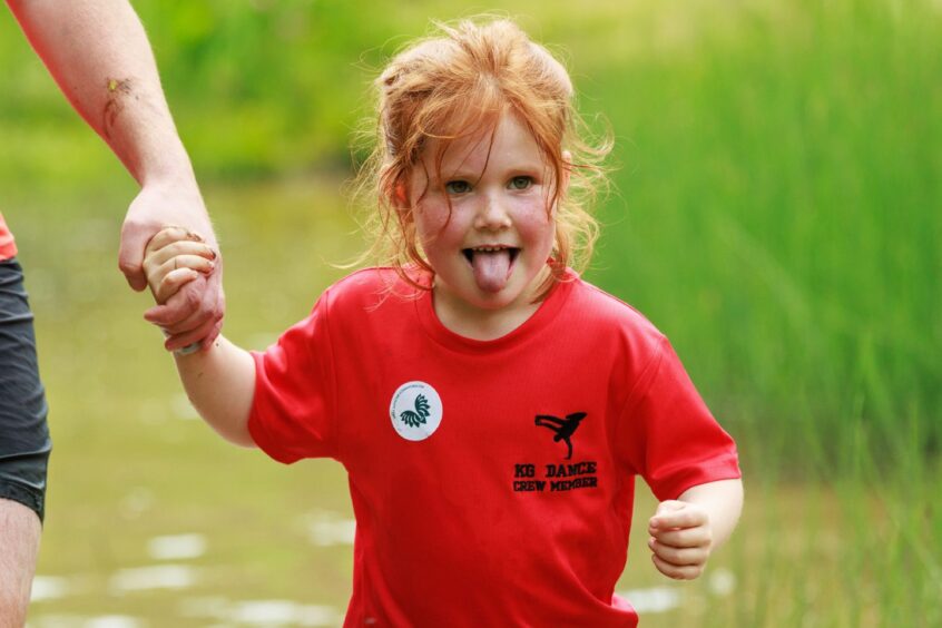 A young girl holds an adult's hand as she wades through a muddy pond. 