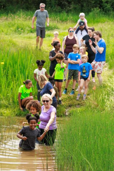 A trio wade through a muddy pond while other participants wait their turn. 