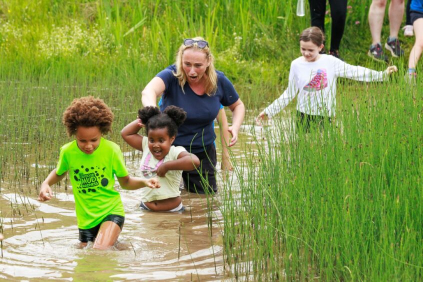 Four participants wade through a muddy pond. 