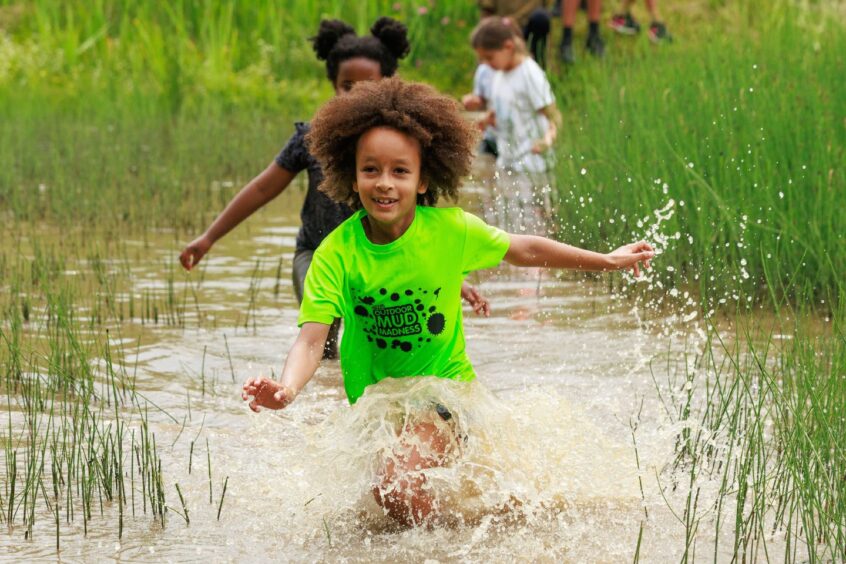 Children wade through a muddy pond. 