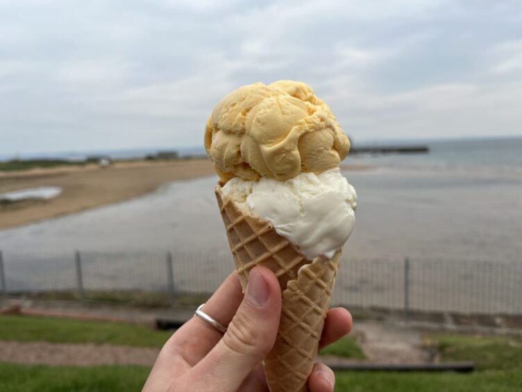 An ice cream cone topped with a scoop of vanilla ice cream and a scoop of mango ice cream.