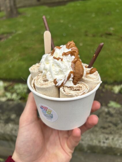 A person holds rolled ice cream served in a tub.
