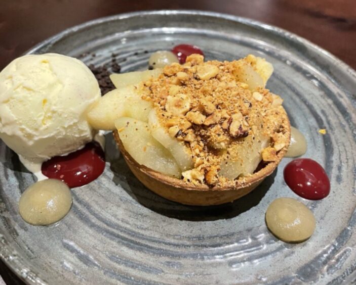 A grey plate with an apple crumble tart and a scoop of vanilla ice cream.