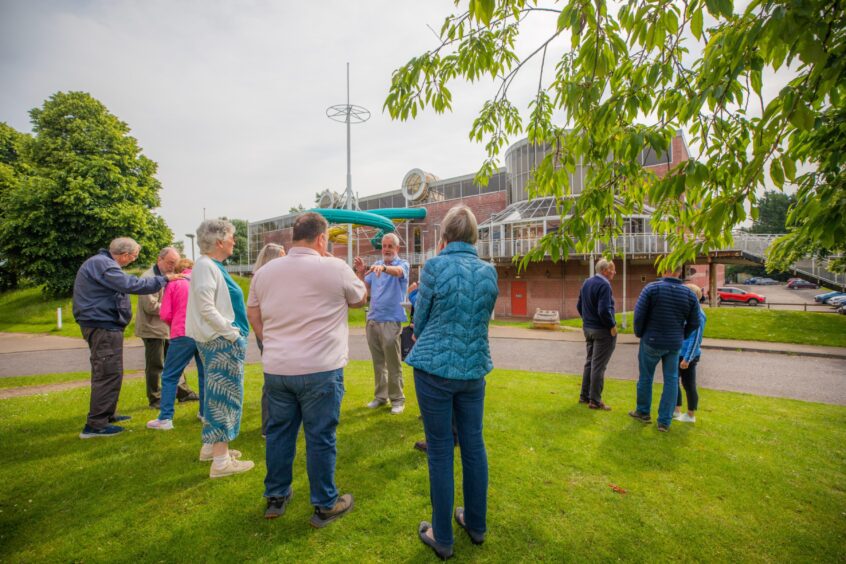 People standing talking on grass with Perth Leisure Pool behind