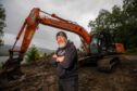 Geoff Mumford, arms folded in black hoodie with long beard, in front of digger in Perthshire countryside