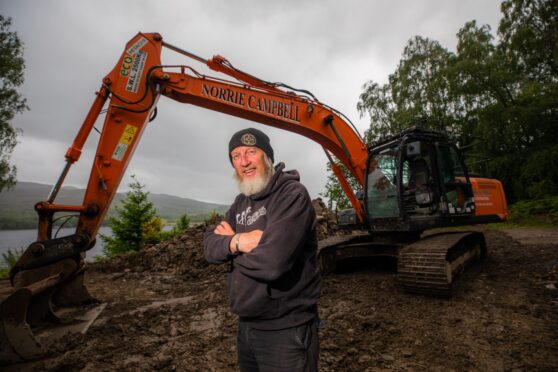 Geoff Mumford, arms folded in black hoodie with long beard, in front of digger in Perthshire countryside