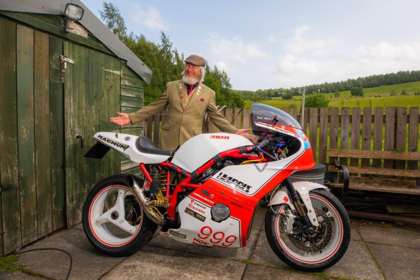 Geoff Mumford smiling beside shiny Harris Magnum motorcycle.