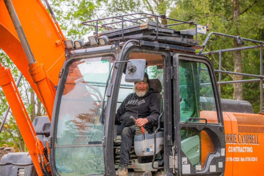 Geoff Mumford at controls of digger in jeans, black hoody and muddy boots