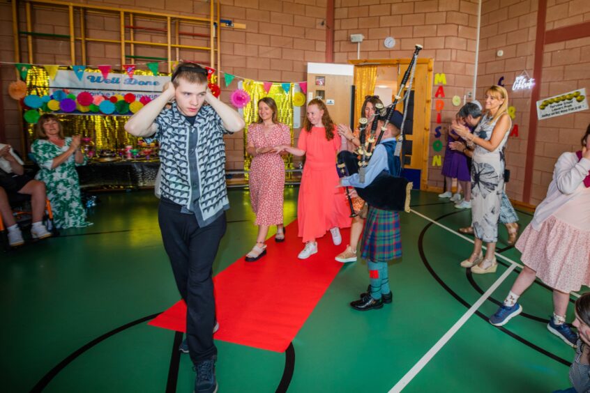 A young piper performs as pupils enter a gym hall. 