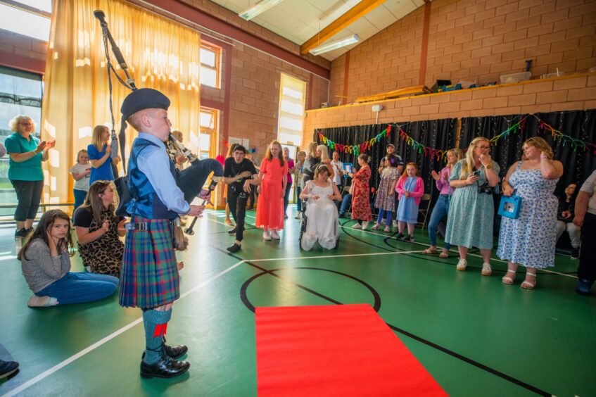 A young piper performs in a gym hall festooned with decorations as party-goers look on. 
