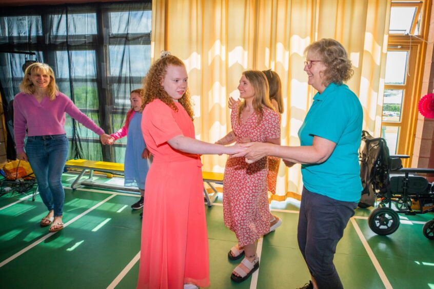 A woman and a girl dancing in a gym hall festooned with decorations. 