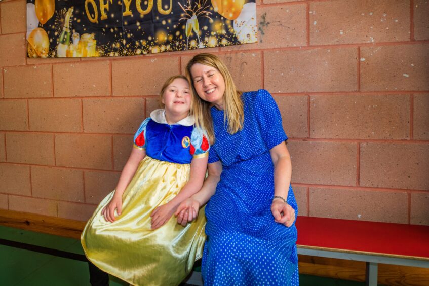 A girl dressed as Disney's Snow White sits with a woman in a blue dress, both smiling. 