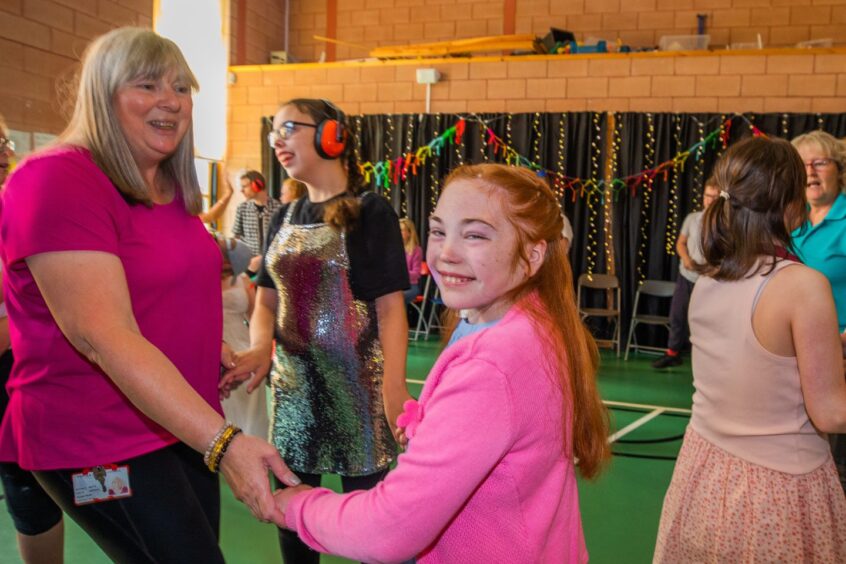 A woman and a girl dancing in a gym hall festooned with decorations. 