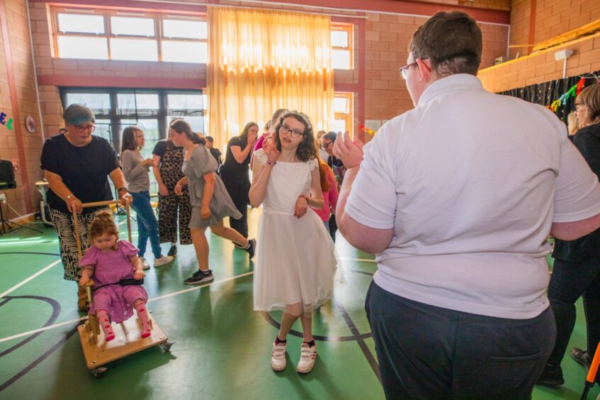 Staff and pupils dancing in a gym hall festooned with decorations. 
