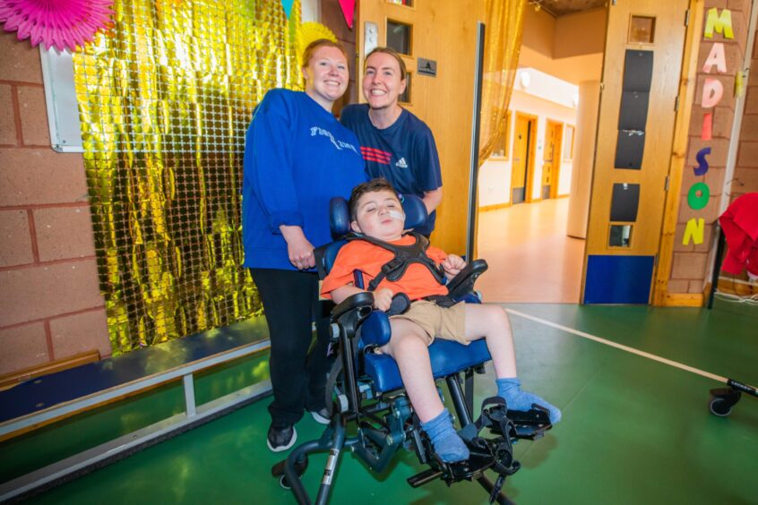 Two smiling women pose with a boy in a wheelchair. 