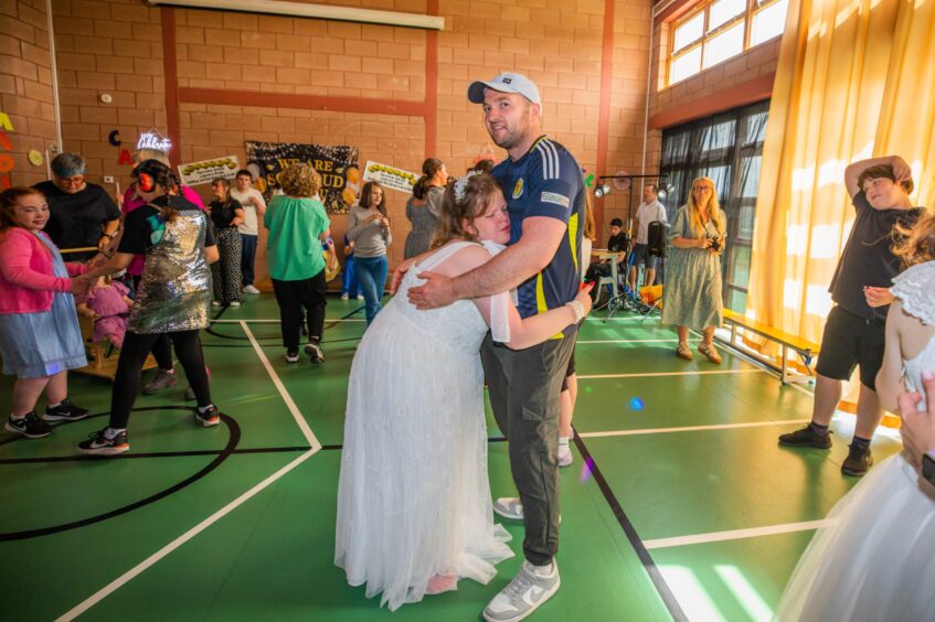 A man and his daughter dancing in a gym hall festooned with decorations. 