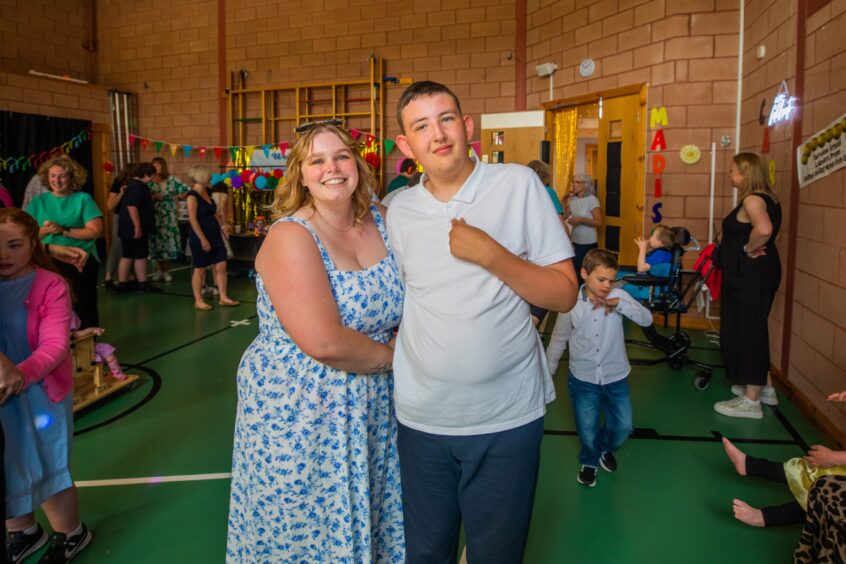 A woman and young man smiling in a gym hall festooned with decorations. 