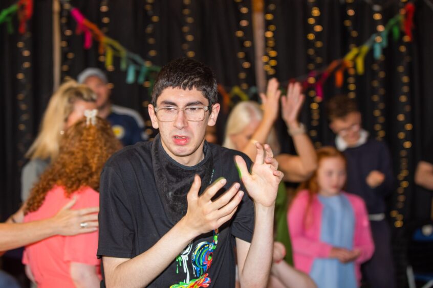 A boy with glasses dancing in a gym hall festooned with decorations. 